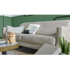 HUKLA® | IL Interliving Serie 4065 2,5-Sitzer-Sofa „Cloudy“ in Kieseloptik mit drei Kissen, Kerze auf dem Tisch, grün-weiße Wand.