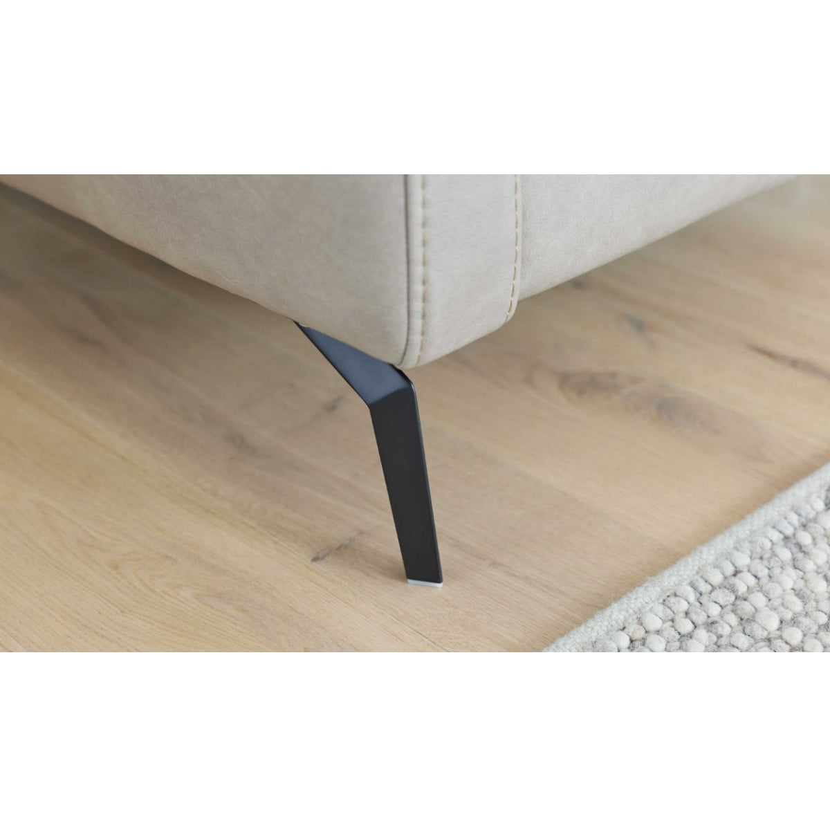 Nahaufnahme eines schwarzen Metallfußes W008-M01, Sofa „Interliving Serie 4065“ von HUKLA® | IL, auf hellem Holzboden mit beigem Teppich.