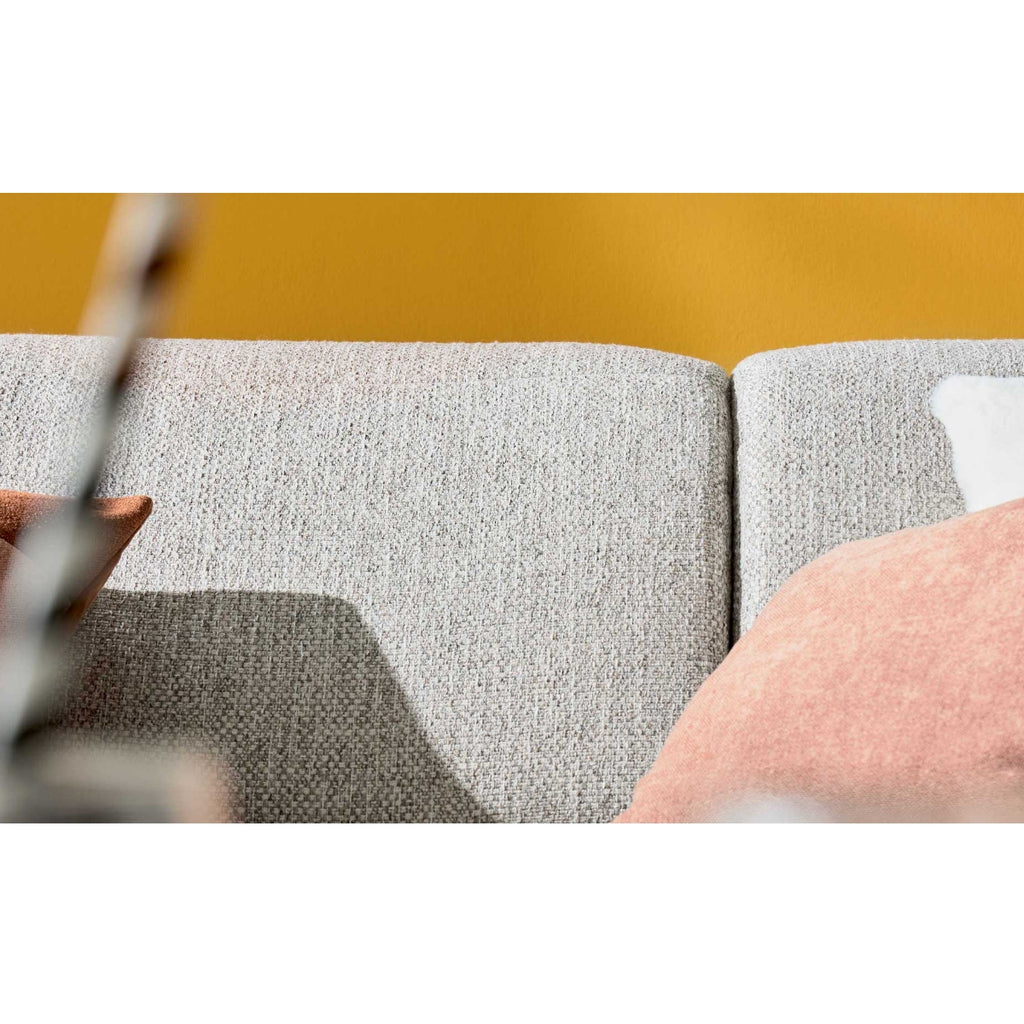 Nahaufnahme des Ecksofas „IL“ von Steinpol Polsteria, Modell Interliving 4460, mit silbernem Stoffbezug, schwarzen, runden Metallfüßen sowie rosa und weißen Kissen.