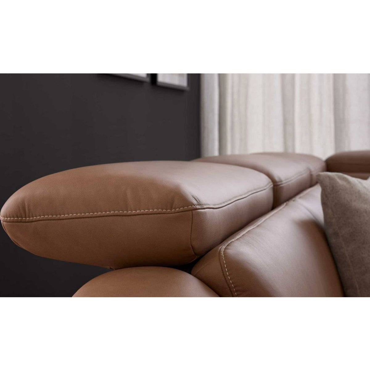 Nahaufnahme eines Leder-Ecksofas von Steinpol Polsteria in Haselnussbraun, mit sichtbaren Nähten an den Kopfstützen, dunkle Wand im Hintergrund.