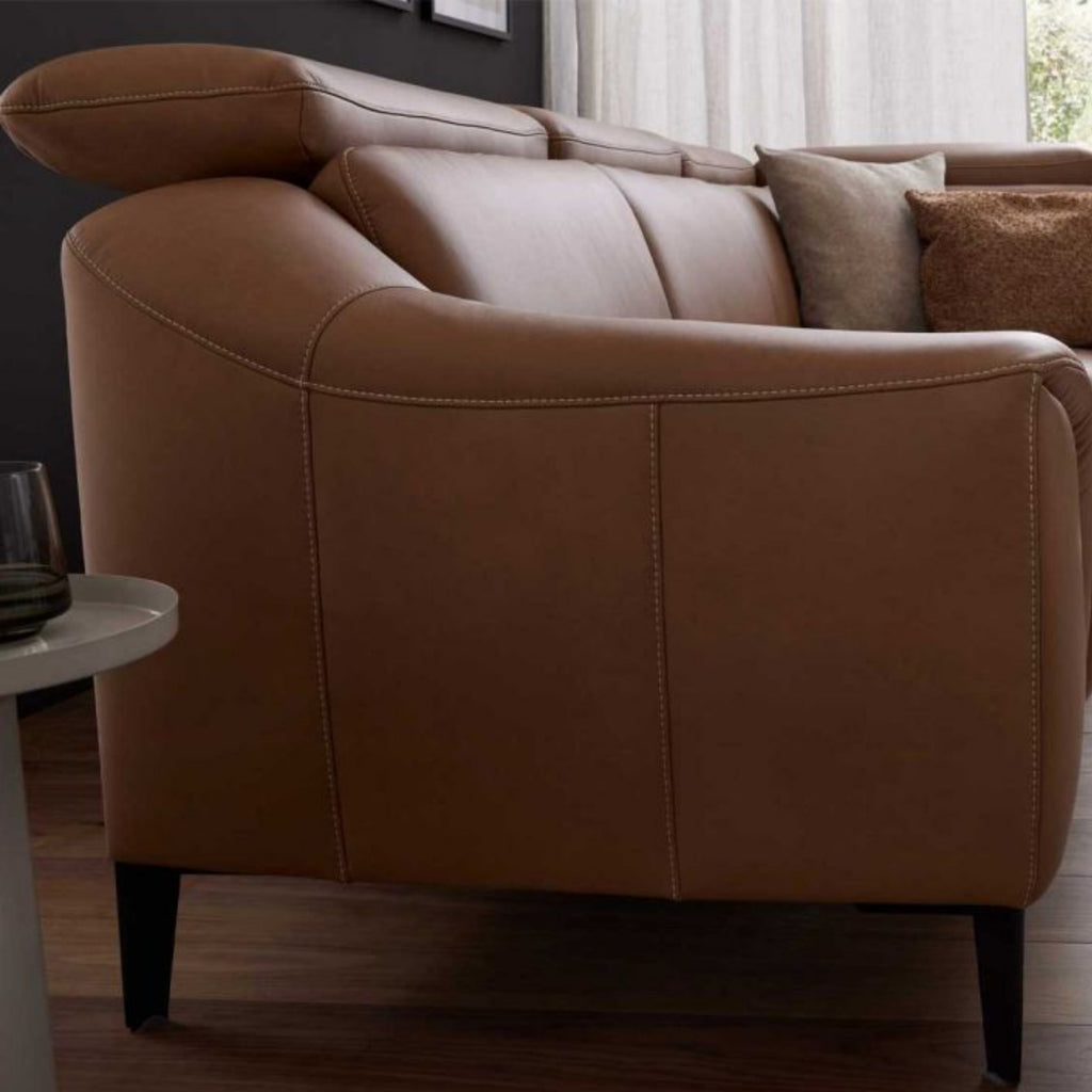 Seitenansicht des Leder-Ecksofas von Steinpol Polsteria in Haselnussbraun, modernes Design, auf einem Holzboden mit beigen Kissen.