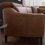 Seitenansicht des Leder-Ecksofas von Steinpol Polsteria in Haselnussbraun, modernes Design, auf einem Holzboden mit beigen Kissen.