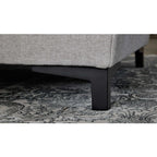Nahaufnahme der Interliving 4700 Eckkombination in der Farbe „Toni Silver“ von HUKLA® auf einem gemusterten Teppich mit schwarzen Beinen.