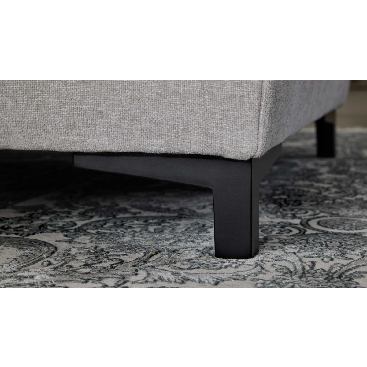 Nahaufnahme der Interliving 4700 Eckkombination in der Farbe „Toni Silver“ von HUKLA® auf einem gemusterten Teppich mit schwarzen Beinen.