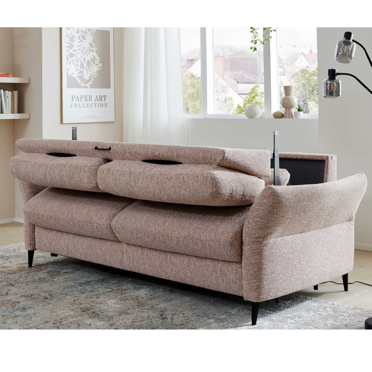 Hellbraunes HUKLA® Interliving Serie 4700 Längsschläfer-Sofa mit verstellbaren Rückenlehnen in einem hellen, mit Teppichen geschmückten Raum.