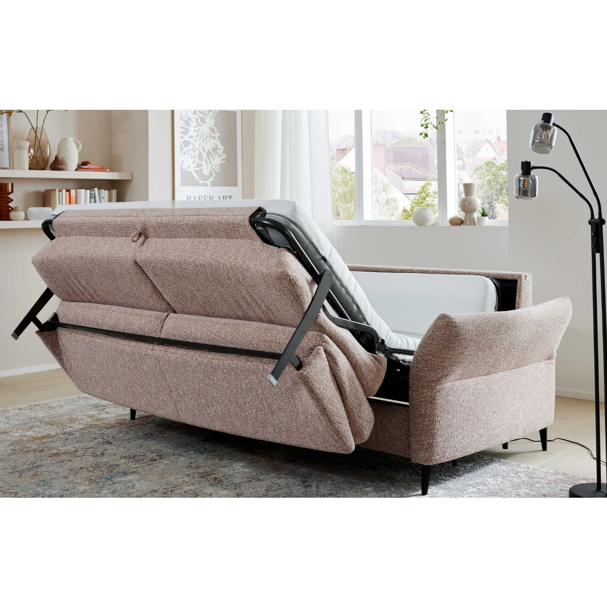 Ein rosa Schlafsofa der Interliving Serie 4700 von HUKLA® steht ausgeklappt in einem hellen Raum mit großen Fenstern und schlichter Einrichtung.