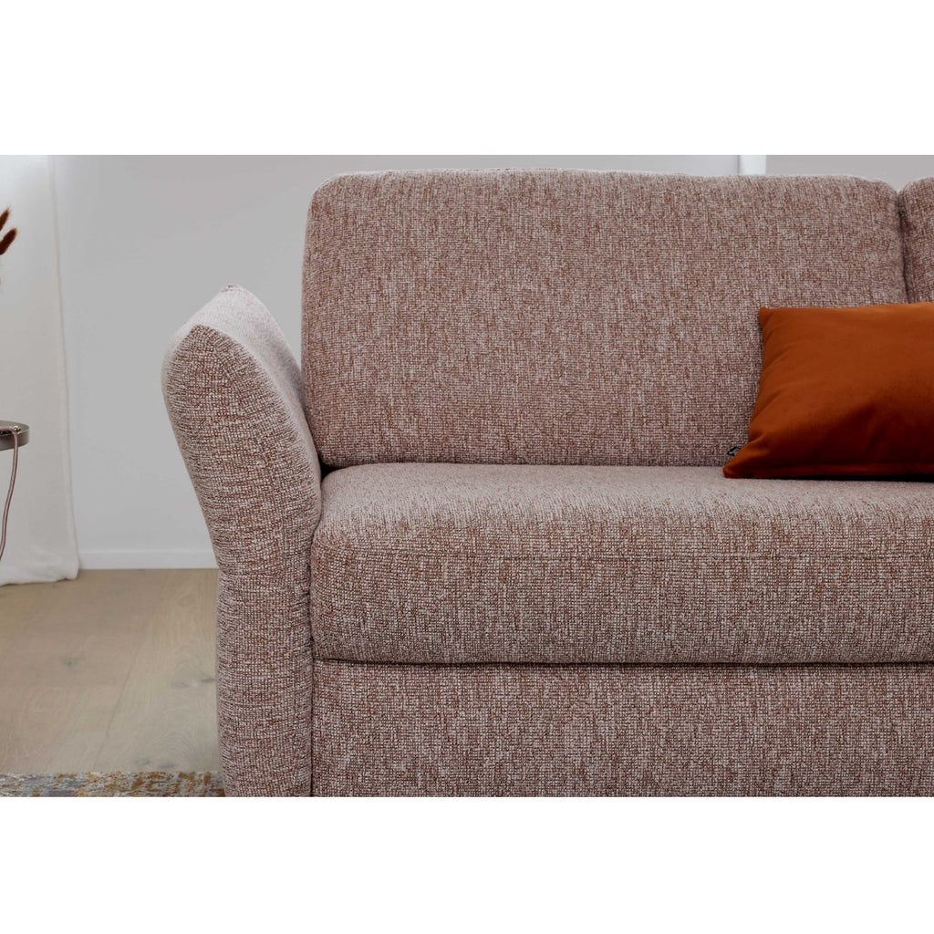 Braunes Sofa der HUKLA® Interliving Serie 4700 mit einer Armlehne, orangefarbenem Kissen und hellem Holzboden im Hintergrund.