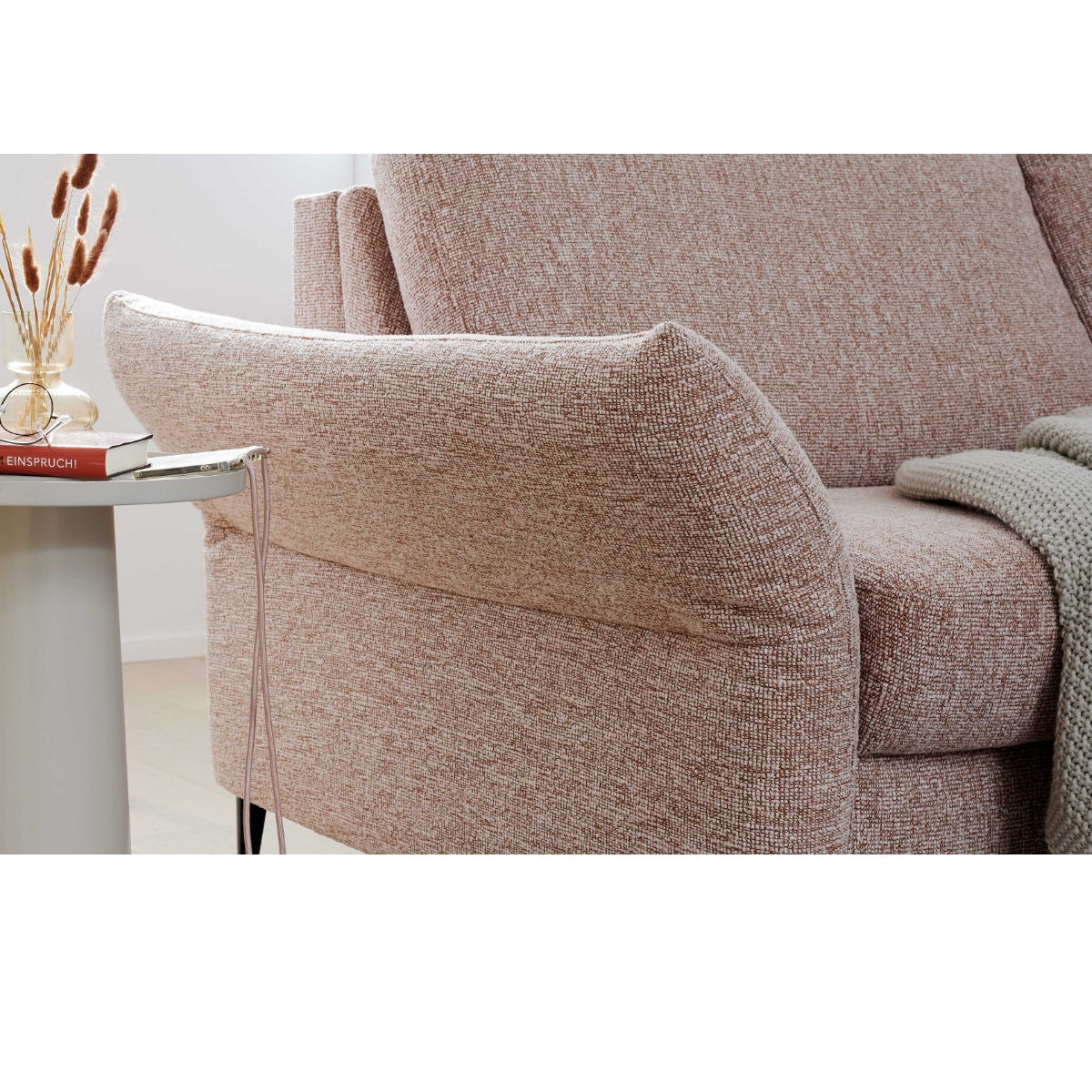 Beiges HUKLA®-Sofa der Serie 4700 in Längsausführung mit Struktur, daneben ein Tisch mit einem Buch, einer Vase und einer drapierten Strickdecke.