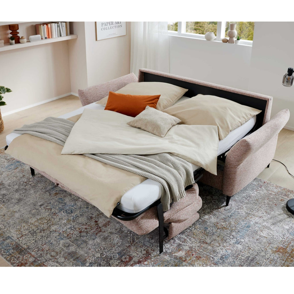 Ein ausgezogenes, beiges Schlafsofa der HUKLA® Comfortbetten Interliving Serie 4700 mit cremefarbener Bettwäsche in einem gemütlichen Wohnzimmer.