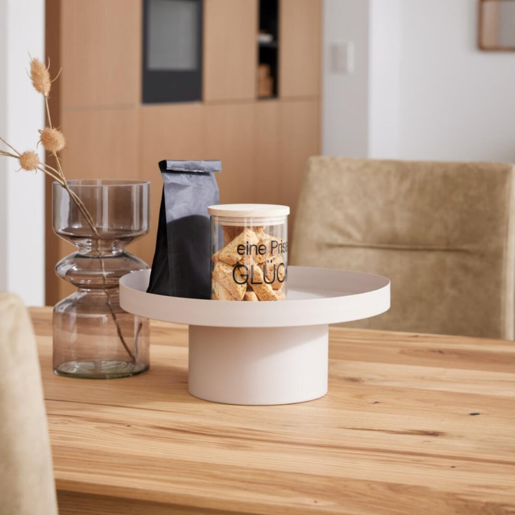Eine Vase, eine schwarze Tasche und eine Keksdose verleihen Ihrem VENJAKOB | IL Interliving 5604 Esstisch in natürlicher Optik einen modernen Touch.
