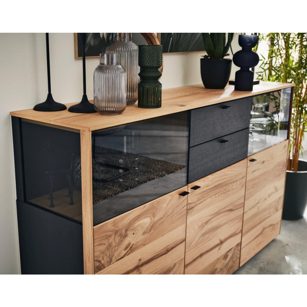 VENJAKOB Interliving Serie 5604 V728-0308 Sideboard, Eiche/Anthrazit, mit Glaselementen neben Grünpflanzen.