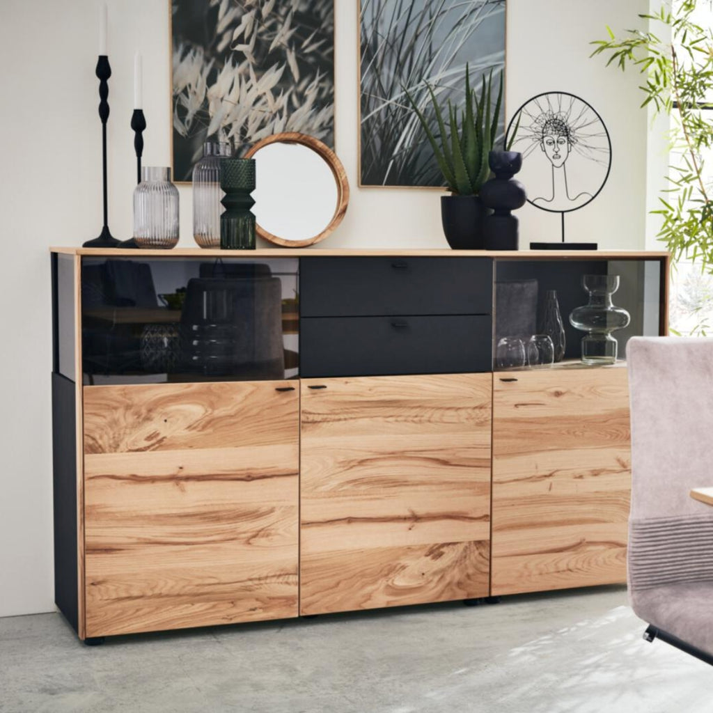 VENJAKOB | IL Interliving Serie 5604 Sideboard aus Eiche, auf dem Vasen, Kerzen, Kunstwerke und Topfpflanzen ausgestellt sind.