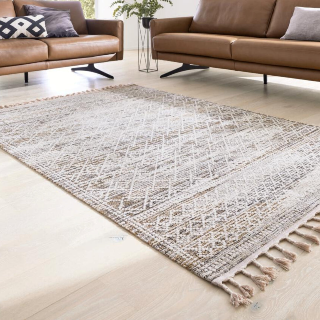 GOLZE | Der Teppich in Beige und Creme mit Rautenmuster und Fransen in einem modernen Wohnzimmer mit braunen Ledersofas.