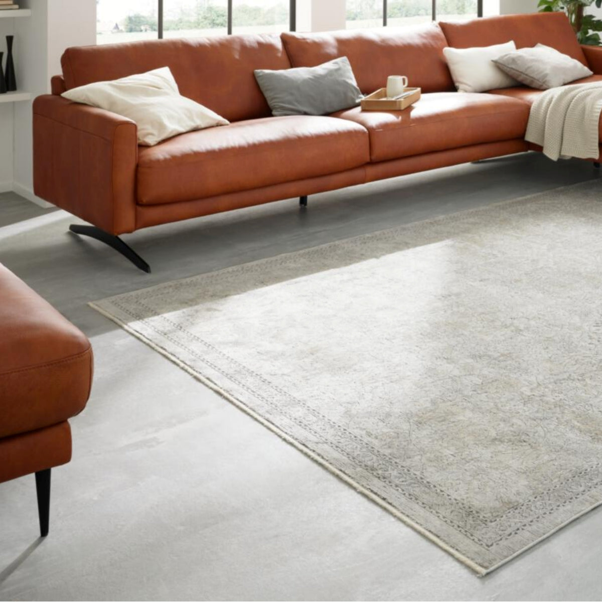 Modernes Wohnzimmer mit Leder-Ecksofa, Kissen in neutralen Farbtönen und einem Teppich von GOLZE | IL Interliving, Modell G-8040, in den Farben Vintage-Beige und Creme.