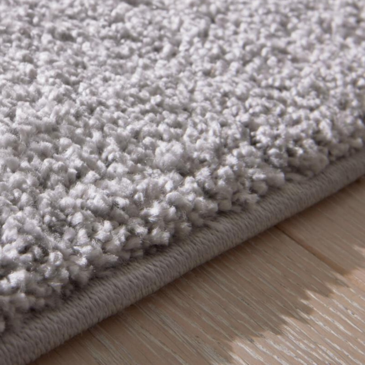 Nahaufnahme des GOLZE | IL Hochflor-Teppichs in elegantem Hellgrau, besonders weich, auf einem hellen Holzboden.