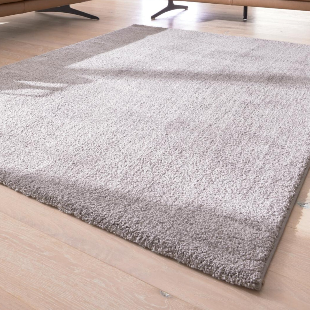 Eleganter hellgrauer Hochflor-Teppich von GOLZE | IL auf Holzboden, Sofaecke sichtbar, aus der Serie G-8080.