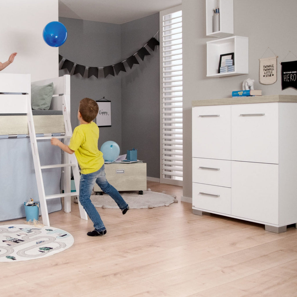 Zwei Kinder spielen mit einem blauen Luftballon in einem modernen Schlafzimmer mit dem PAIDI Kira-Hochregal in Kreideweiß/Eiche-Nebraska.