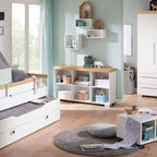 Modernes Kinderzimmer mit dem PAIDI Kira-Sideboard in Kreideweiß/Eiche, Regalen, einem weichen Teppich und Spielzeug auf einem Rolltisch.