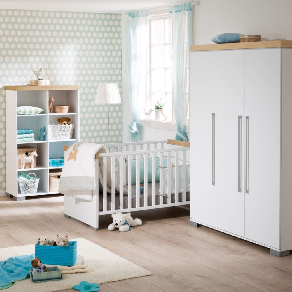 Modernes Kinderzimmer mit einem 0190 PAIDI Kira-Babybett, Spielzeug, blauen Akzenten, hellen Holzböden und Wänden mit Polka-Dot-Muster.