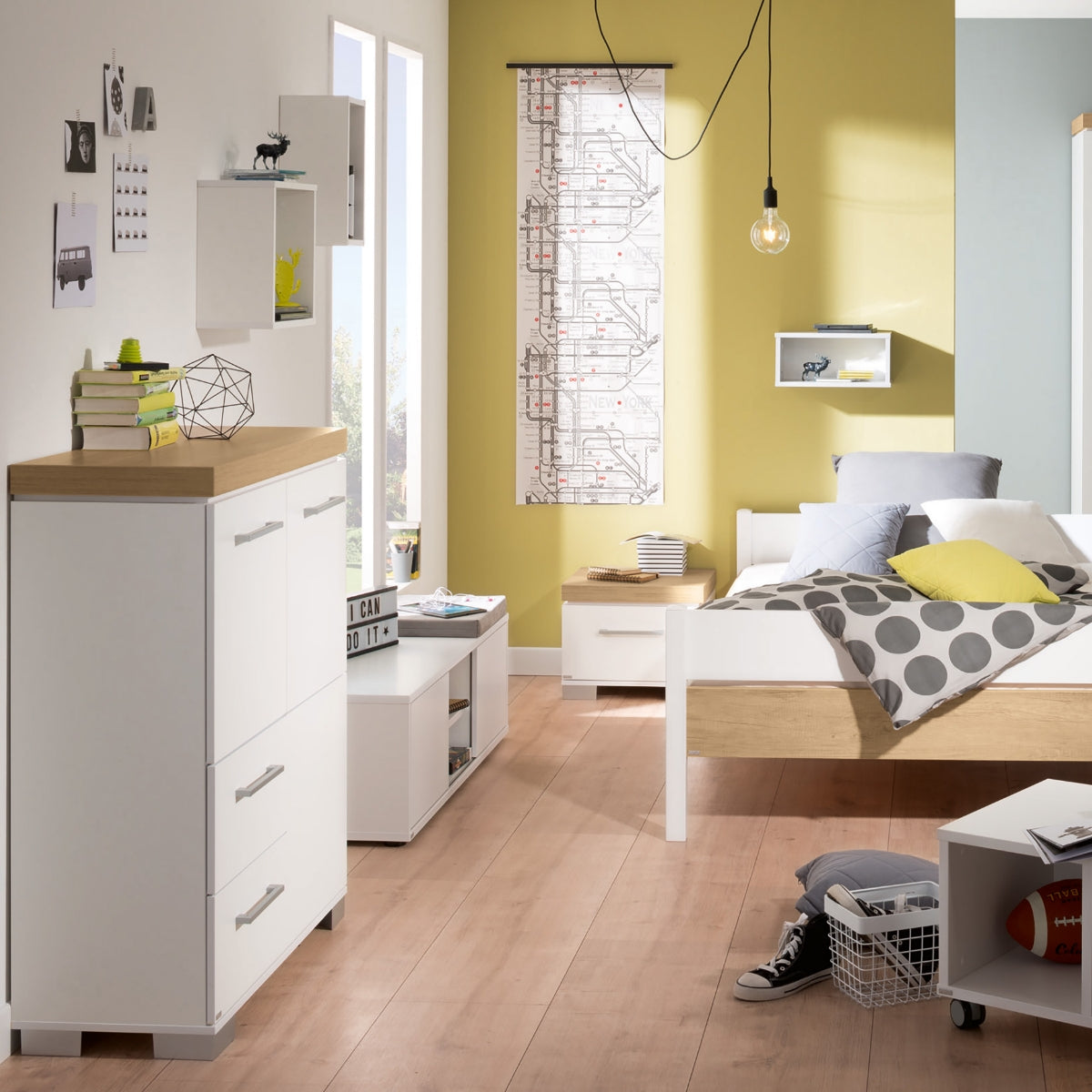 Modernes Schlafzimmer mit weißem PAIDI Kira-Hochschrank, gelber Akzentwand, Deko, Sportausrüstung und Holzboden.