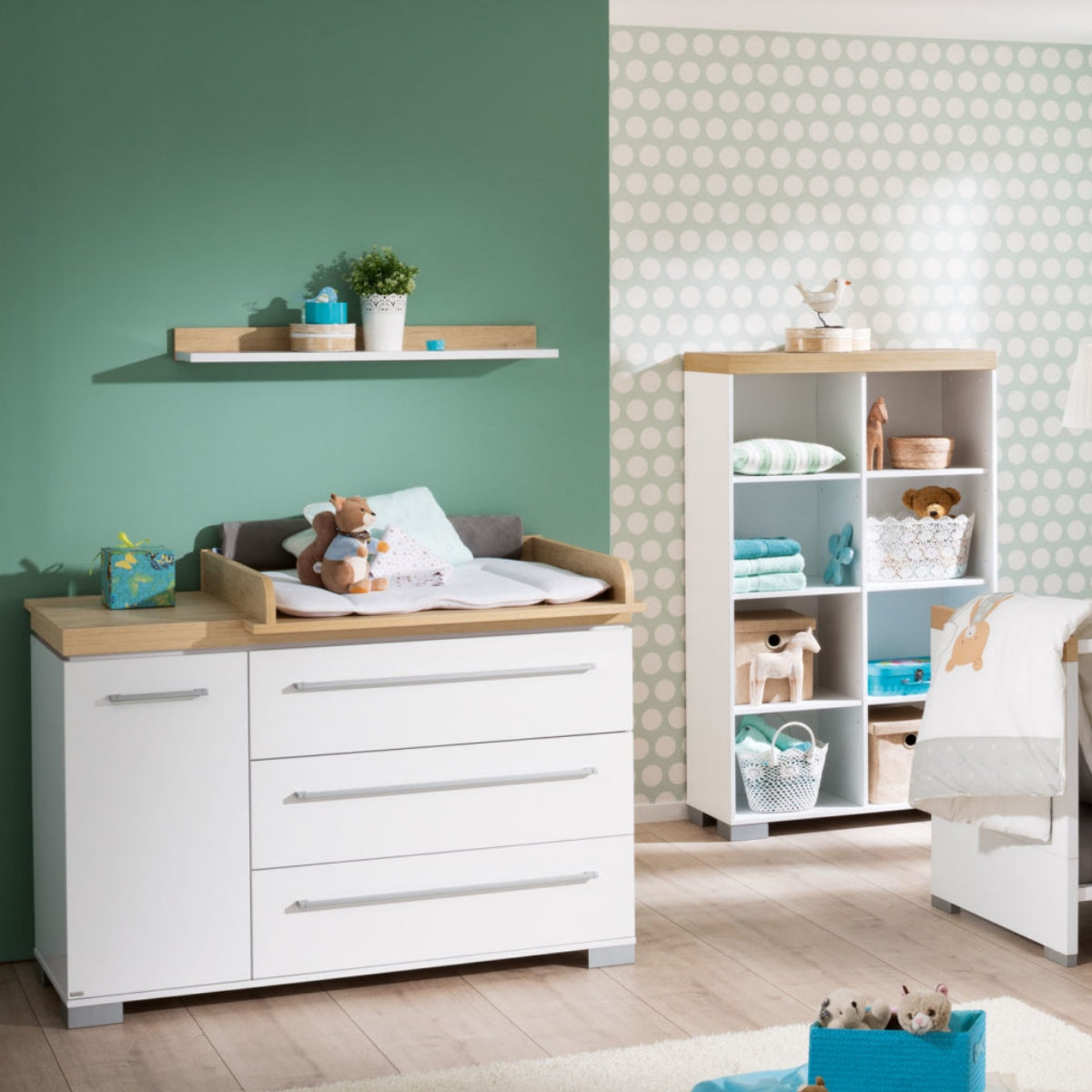Modernes Babyzimmer mit grün gepunkteten Wänden, einer PAIDI Kira Kommode von 0190, Regalen und ordentlich sortiertem Spielzeug.