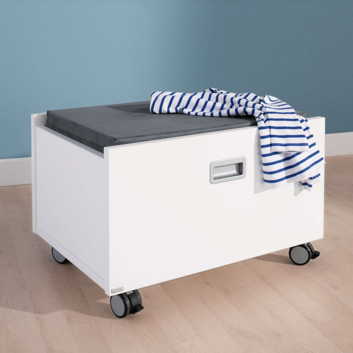 Eine PAIDI Kira Rollbox ohne Polster und in verschiedenen Farben verleiht dem Kinderzimmer unter einem blau gestreiften Hemd einen stilvollen Akzent.