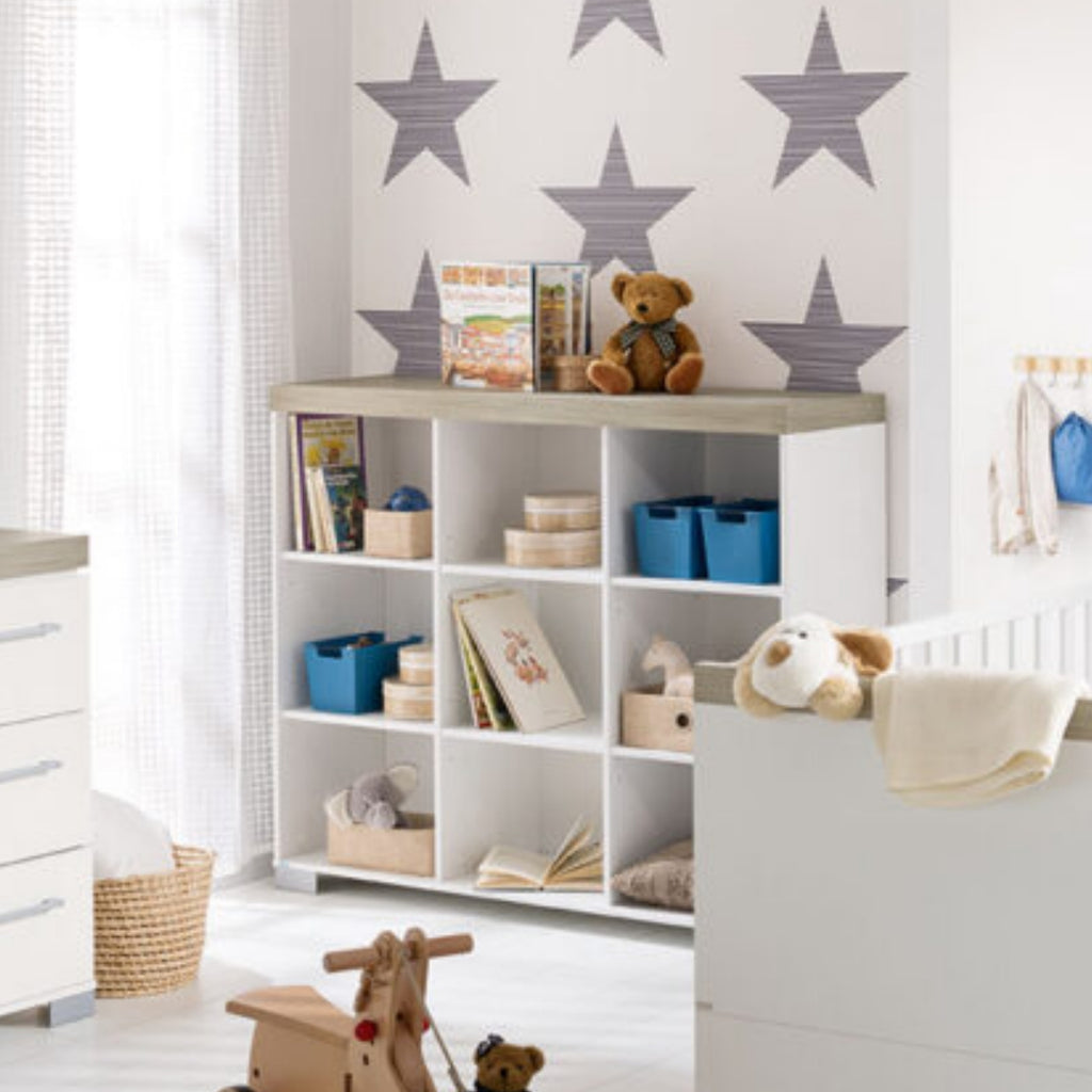 Kinderzimmer mit einem PAIDI-Modell „Kira“ Standregal 0190, Fächerregalen, Spielzeug, Büchern, Sternentapete und einem Teddybär oben drauf.