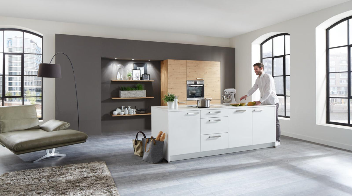 Moderne Küche mit einer Nolte®-Einbauküche „Soft Lack“, AEG-Einbaugeräten, einer Kücheninsel, großen Fenstern und offenen Regalen.