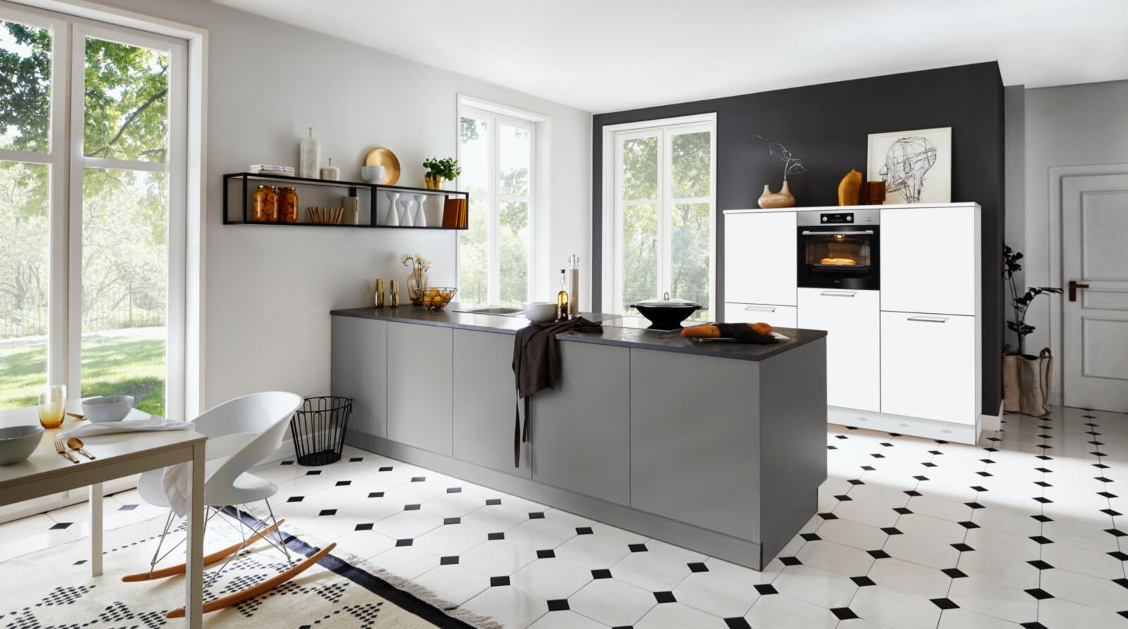 Nolte® Einbauküche „Feel“ mit AEG-Geräten, grauen Schränken, schwarzen Arbeitsplatten und gemustertem Fliesenboden.