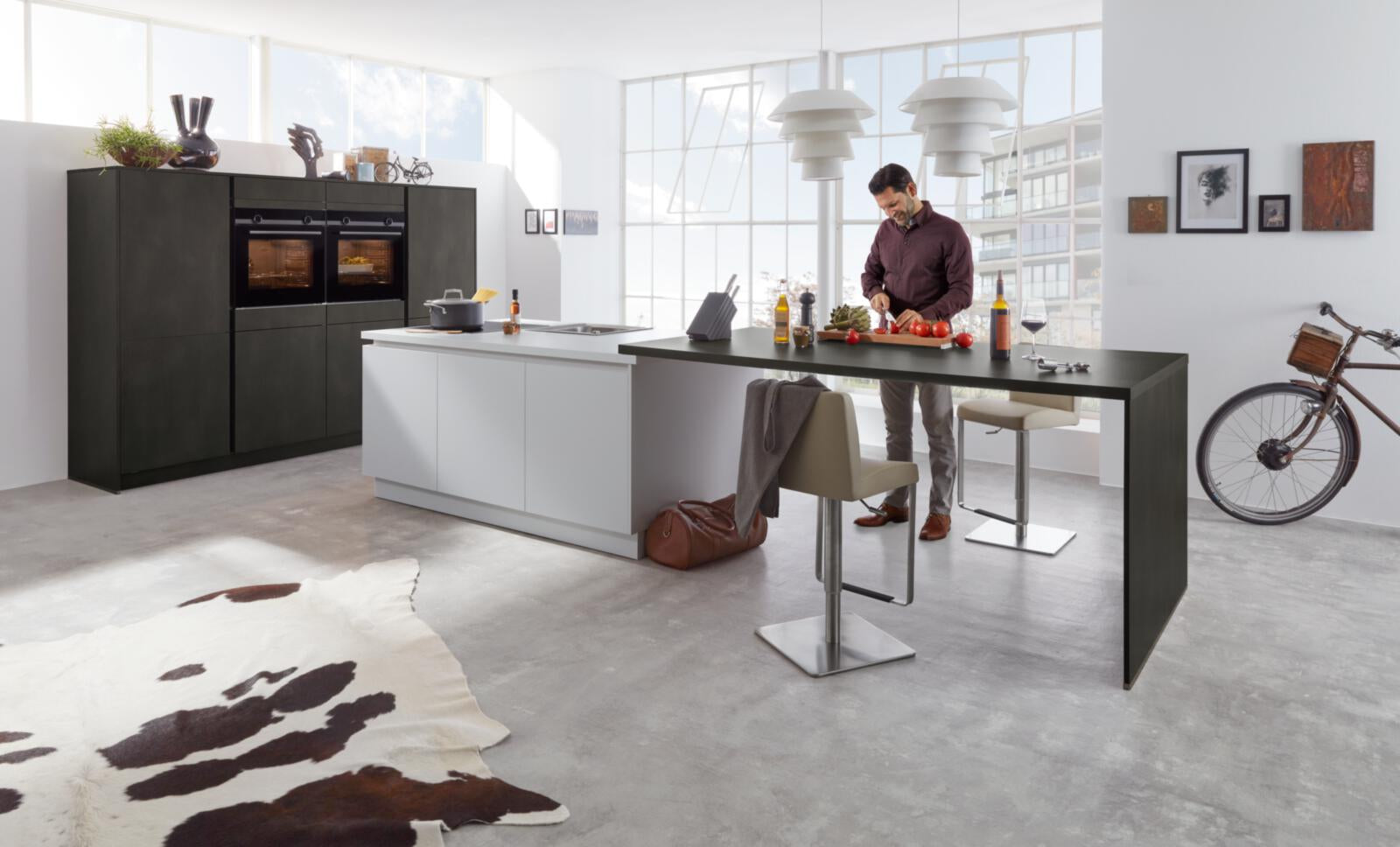 Ein Mann schneidet Gemüse in einer WERT KÜCHE® Nova mit SIEMENS-Einbaugeräten – modernes, griffloses Küchendesign am Fenster.