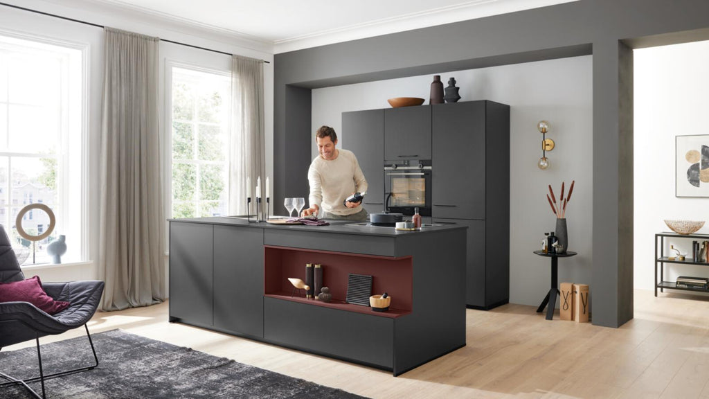 Jemand kocht in einer WERT KÜCHE® Nora von schüller – elegantes Schwarz, warme Akzente, Siemens-Geräte, ein lichtdurchfluteter Raum.