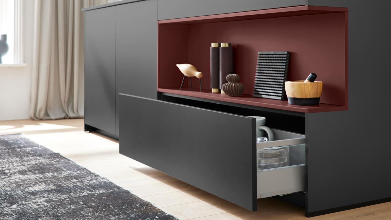 Die elegante WERT KÜCHE® Nora von Schüller: schwarzes Design, rote Akzente, offene Schublade und Einbaugeräte von Siemens für einen modernen Look.