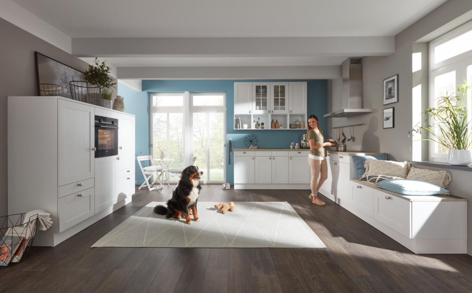 Eine Frau steht mit ihrem Hund in einer Küche von WERT KÜCHE® Carolin mit SIEMENS-Einbaugeräten; auf dem Boden liegen Spielsachen.