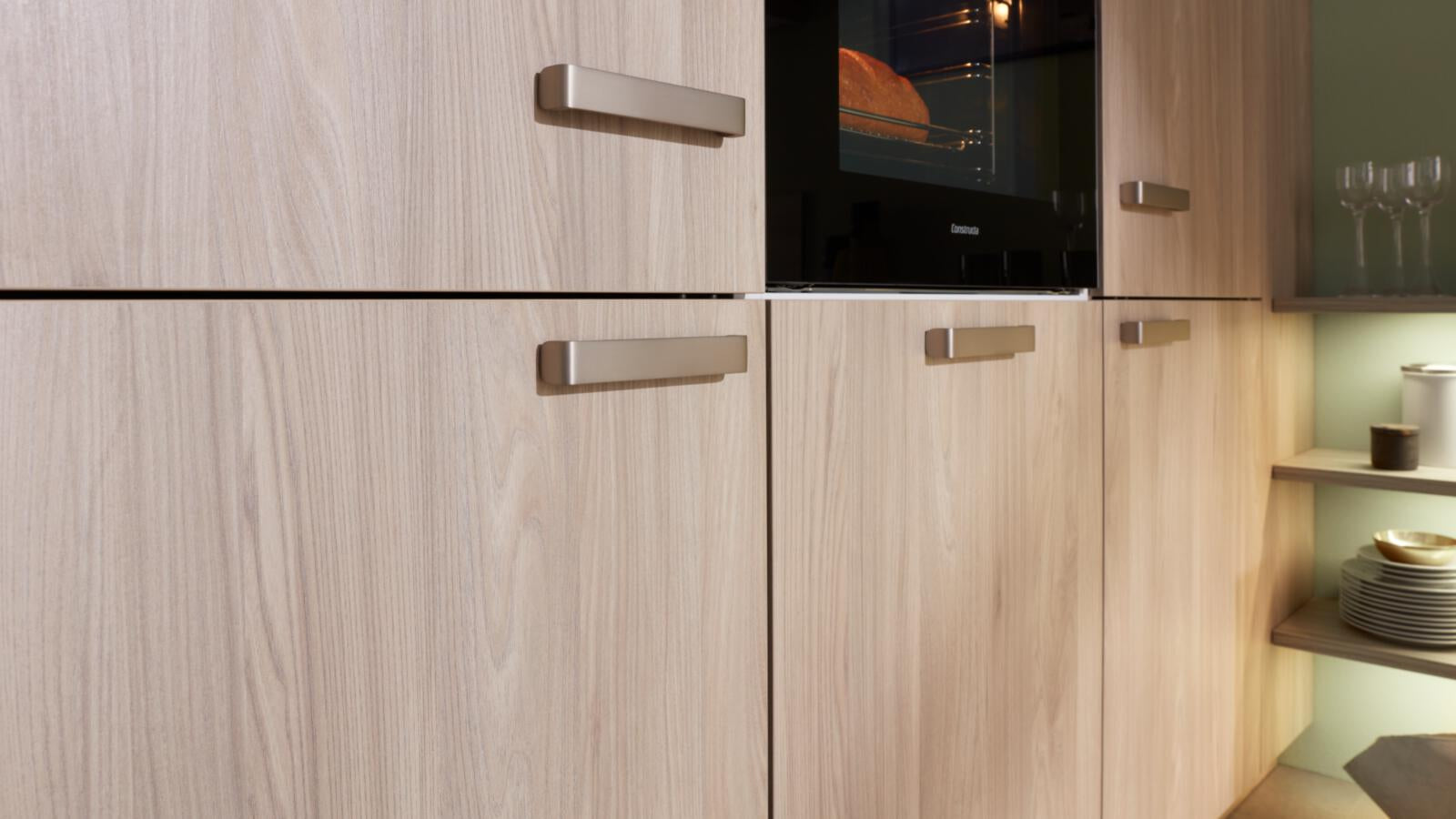 WERT KÜCHE® Mona: Helle Küchenschränke im nordischen Stil, silberne Griffe, Constructa-Backofen und offene Regale auf der rechten Seite.