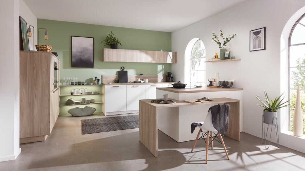 Moderne Küche mit grüner Wand, Schränken in „Nordic Eiche“, offenen Regalen und einem Arbeitsbereich „WERT KÜCHE® Mona by schüller“.