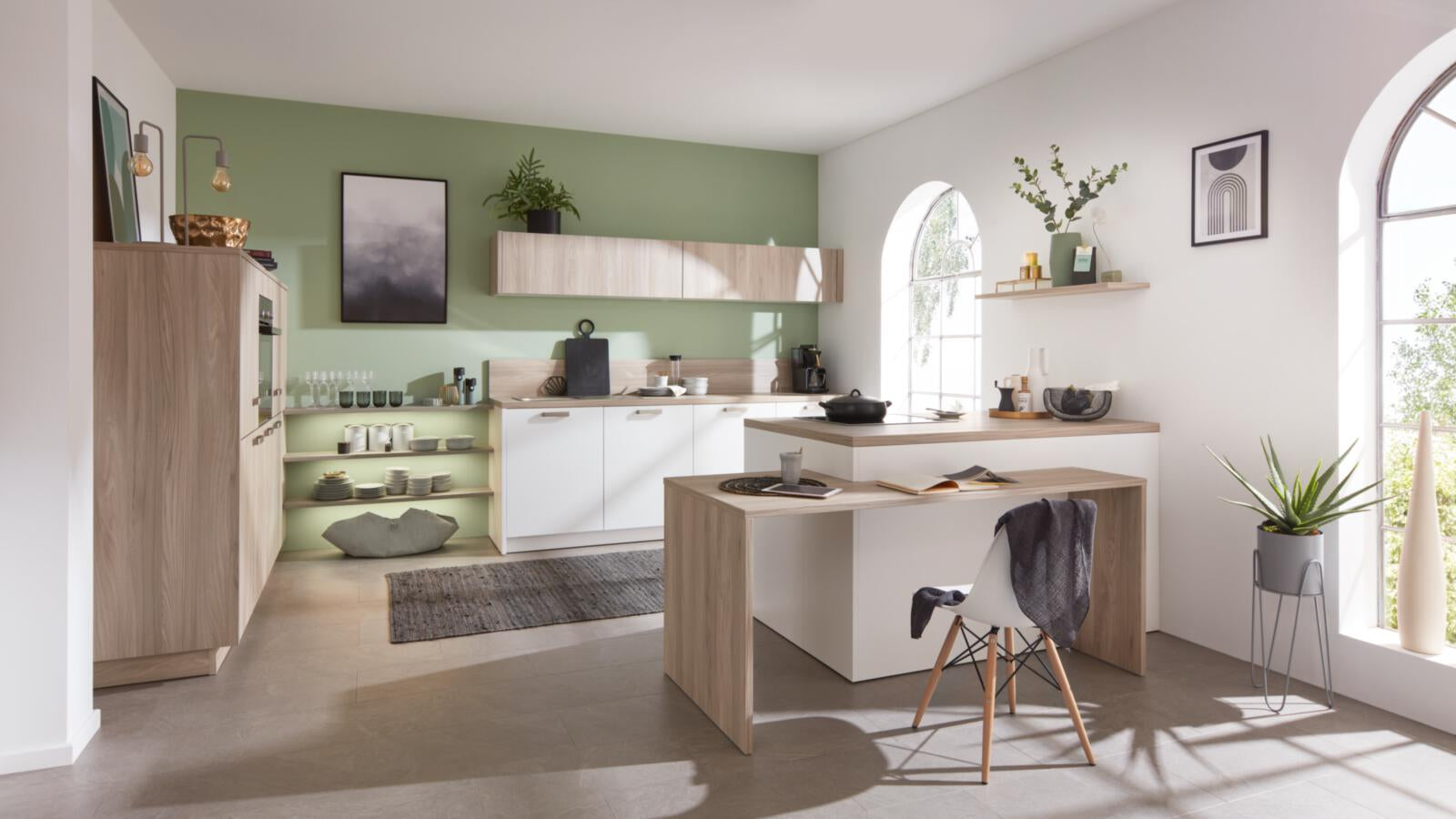 Moderne Küche mit grüner Wand, Schränken in „Nordic Eiche“, offenen Regalen und einem Arbeitsbereich „WERT KÜCHE® Mona by schüller“.