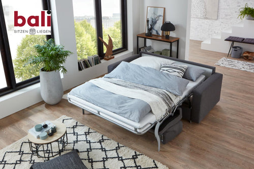 Bali Messina Funktionssofa – Ausgeklapptes Schlafsofa mit Bettwäsche in einem modernen Zimmer, Bali-Logo in der Ecke.