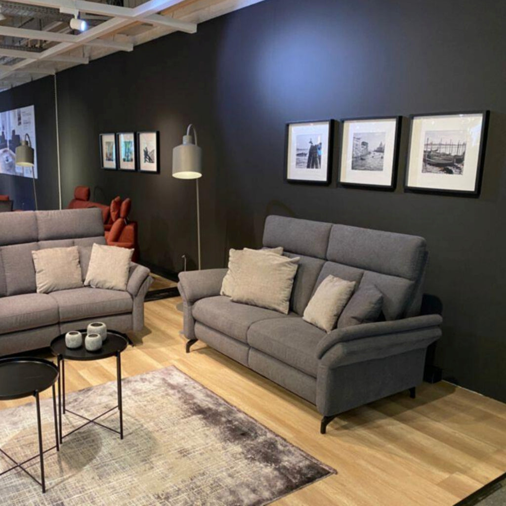 Modernes Wohnzimmer mit einem grauen Zweisitzer „OrthoSedis 4.0“ von Steinpol Polsteria, Wandbildern, einer Stehlampe, Tischen und einem Teppich.