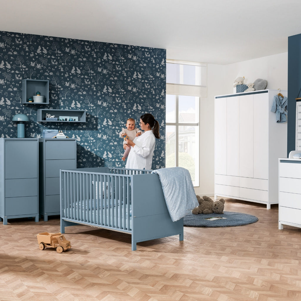 Eine Frau hält ein Baby im blauen PAIDI-Kinderzimmer mit der Oscar-Wandbox und dem Regal mit Stauraum von PAIDI im Arm.
