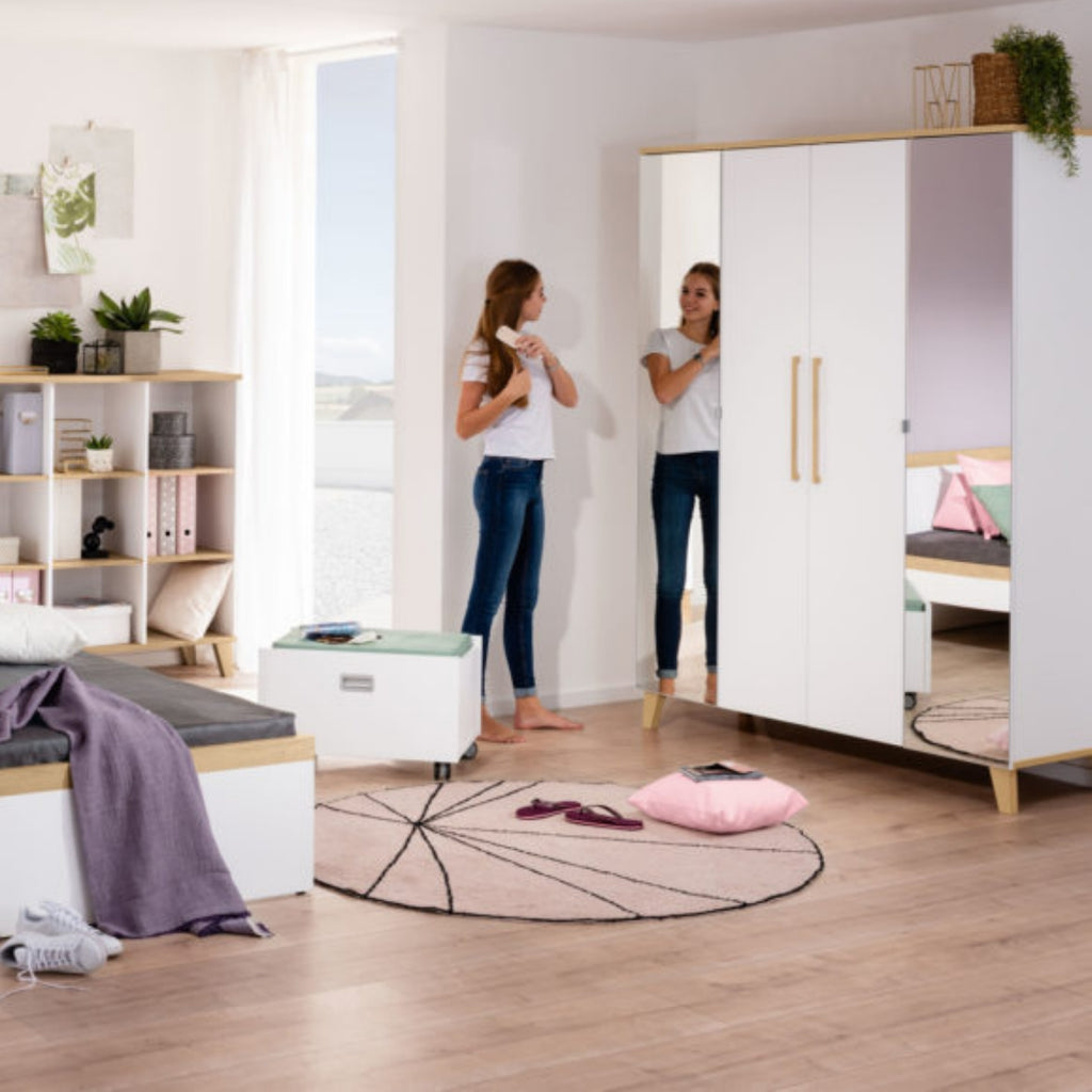 Ein Teenager-Mädchen kämmt sich die Haare – aus dem PAIDI Babyzimmerprogramm „Oscar“ – Kleiderschrank in einem aufgeräumten Jugendzimmer in Pastelltönen.