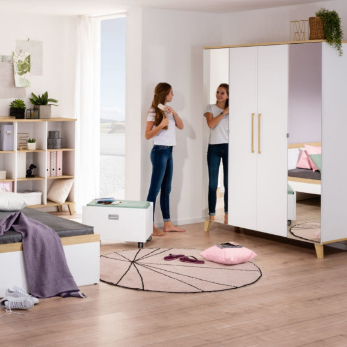 Ein Teenager-Mädchen kämmt sich die Haare – aus dem PAIDI Babyzimmerprogramm „Oscar“ – Kleiderschrank in einem aufgeräumten Jugendzimmer in Pastelltönen.