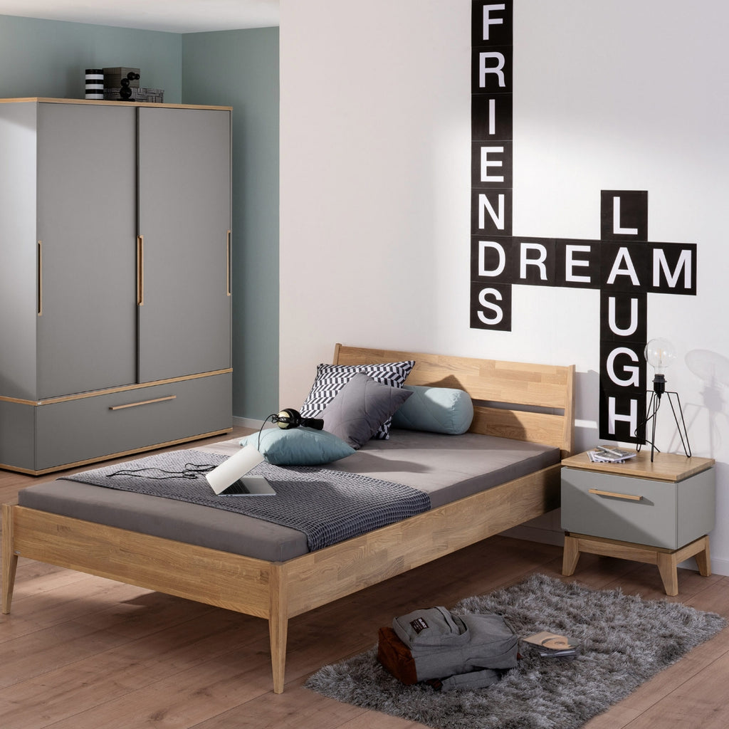 Modernes Schlafzimmer mit der Nachtkommode „Sten“ aus der PAIDI-Jugendzimmer-Serie in Schiefergrau, Eiche und mit dem Kunstdruck „FRIENDS DREAM LAUGH“.