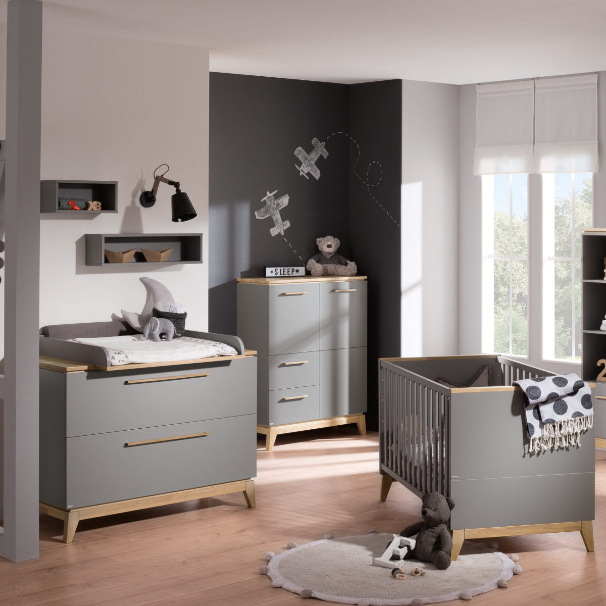 Modernes Kinderzimmer mit dem PAIDI Babyzimmer Sten – Babybettgestell, graues Babybett, Teddybären, Flugzeug-Wandbild und sanftem Fensterlicht.