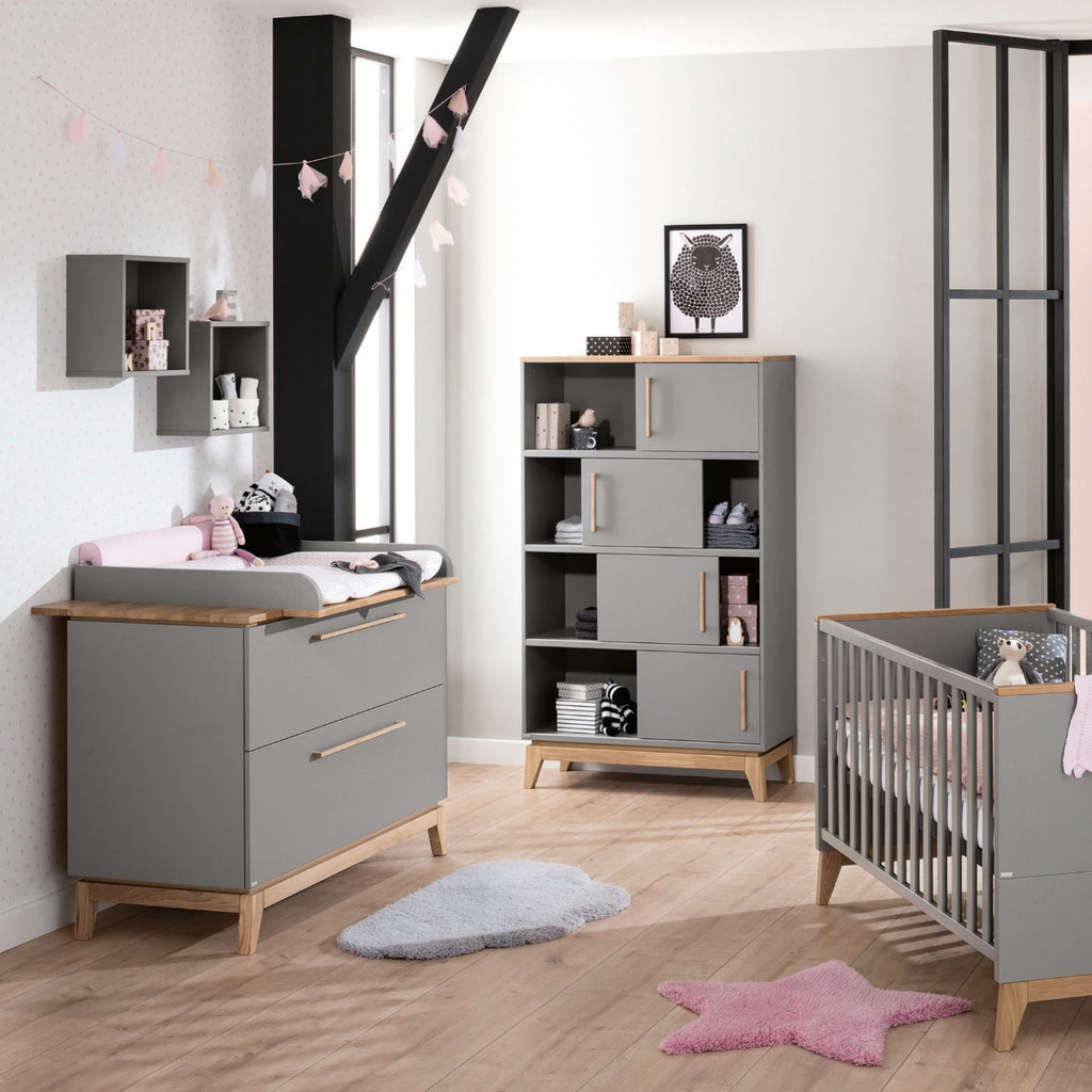 Modernes Kinderzimmer mit der PAIDI-Wickelkommode „Sten“ – graue Möbel, flauschige Teppiche und rosa Deko.