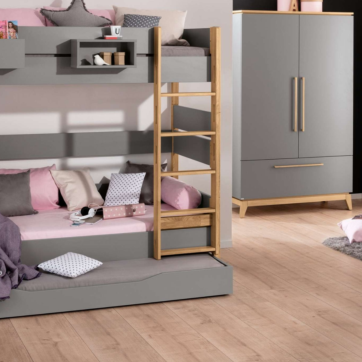 Graues Etagenbett mit rosa-grauer Bettwäsche, Holzleiter und dem PAIDI-Kleiderschrank „Sten“ in einem aufgeräumten Schlafzimmer aus hellem Holz.