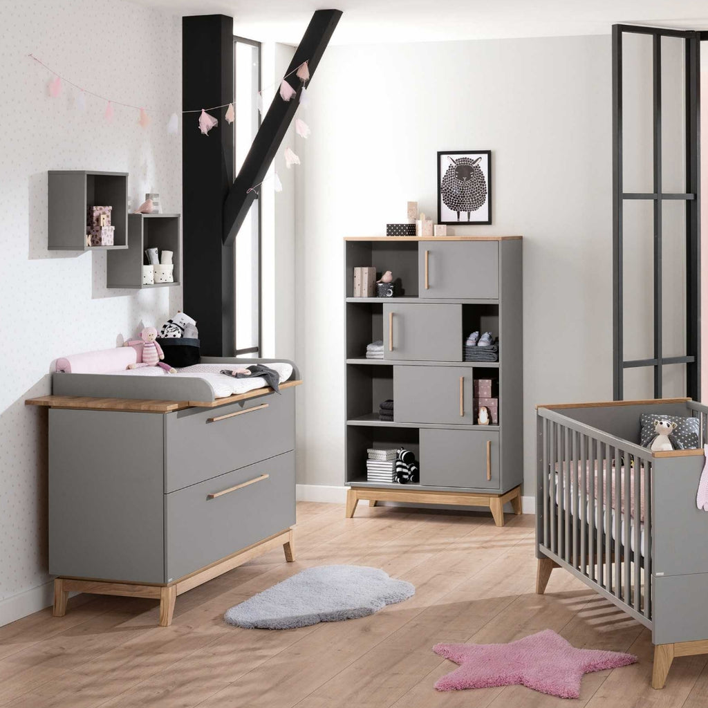 Modernes Kinderzimmer mit grauen Möbeln, einem Kinderbett, dem PAIDI-Stauraumelement „Sten“, Spielzeug und einer Dekoration in Pastelltönen auf Holzböden.