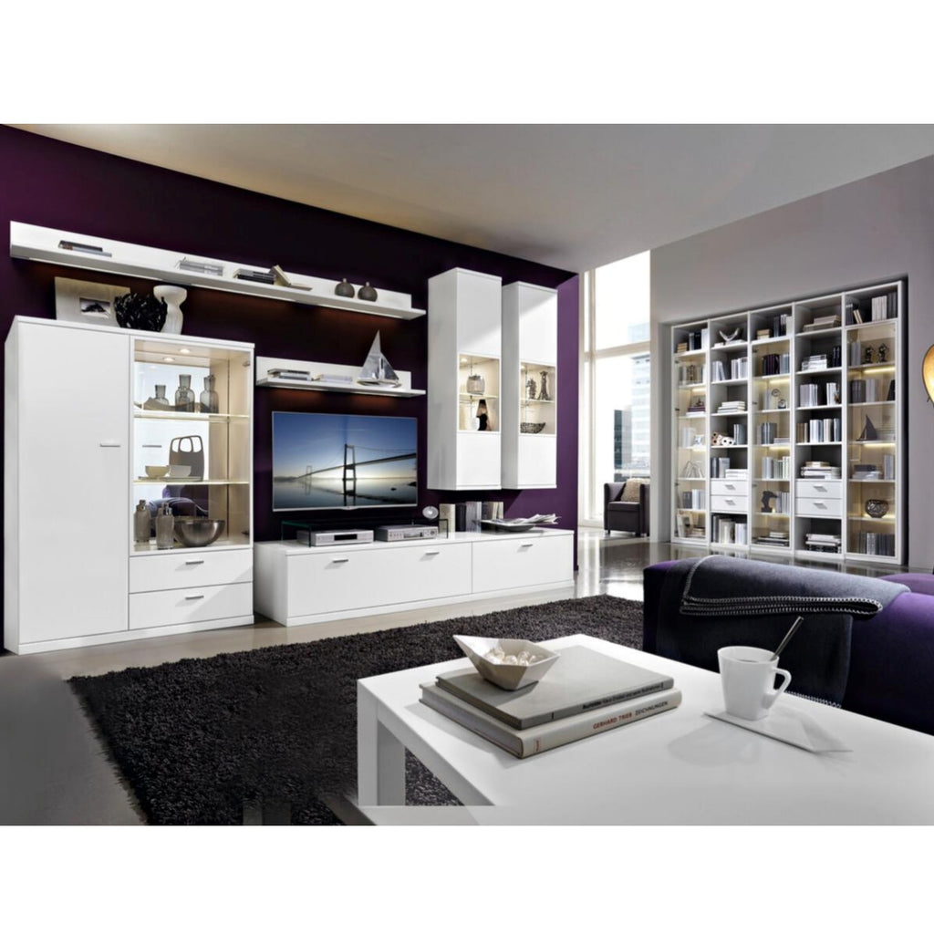 Modernes Wohnzimmer mit Möbeln in Mattweiß, einem dunklen Teppich, einem Fernseher und dem Wohnregal „Vancouver“ von RIETBERGER MÖBELWERKE RMW neben dem Couchtisch.