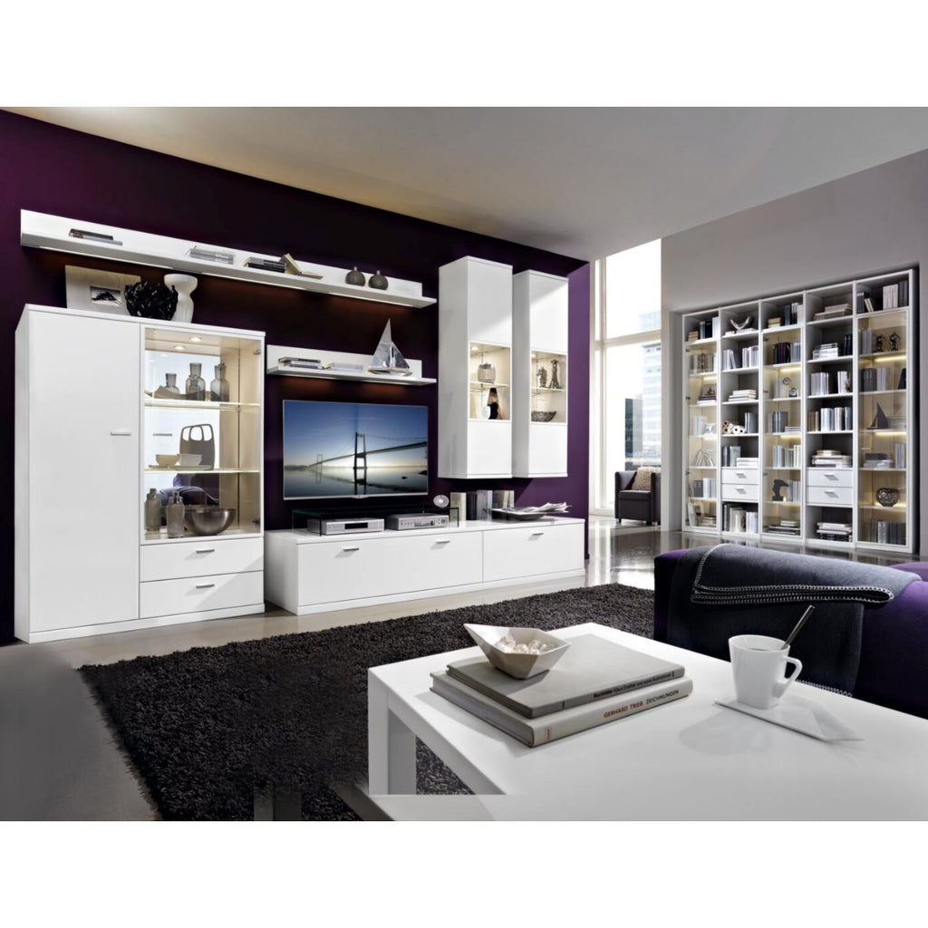 Modernes Wohnzimmer mit der Wohnkombination „RMW Vancouver“, weißen Möbeln, Fernseher, Regalen, Deko, schwarzem Teppich und lila Wand.