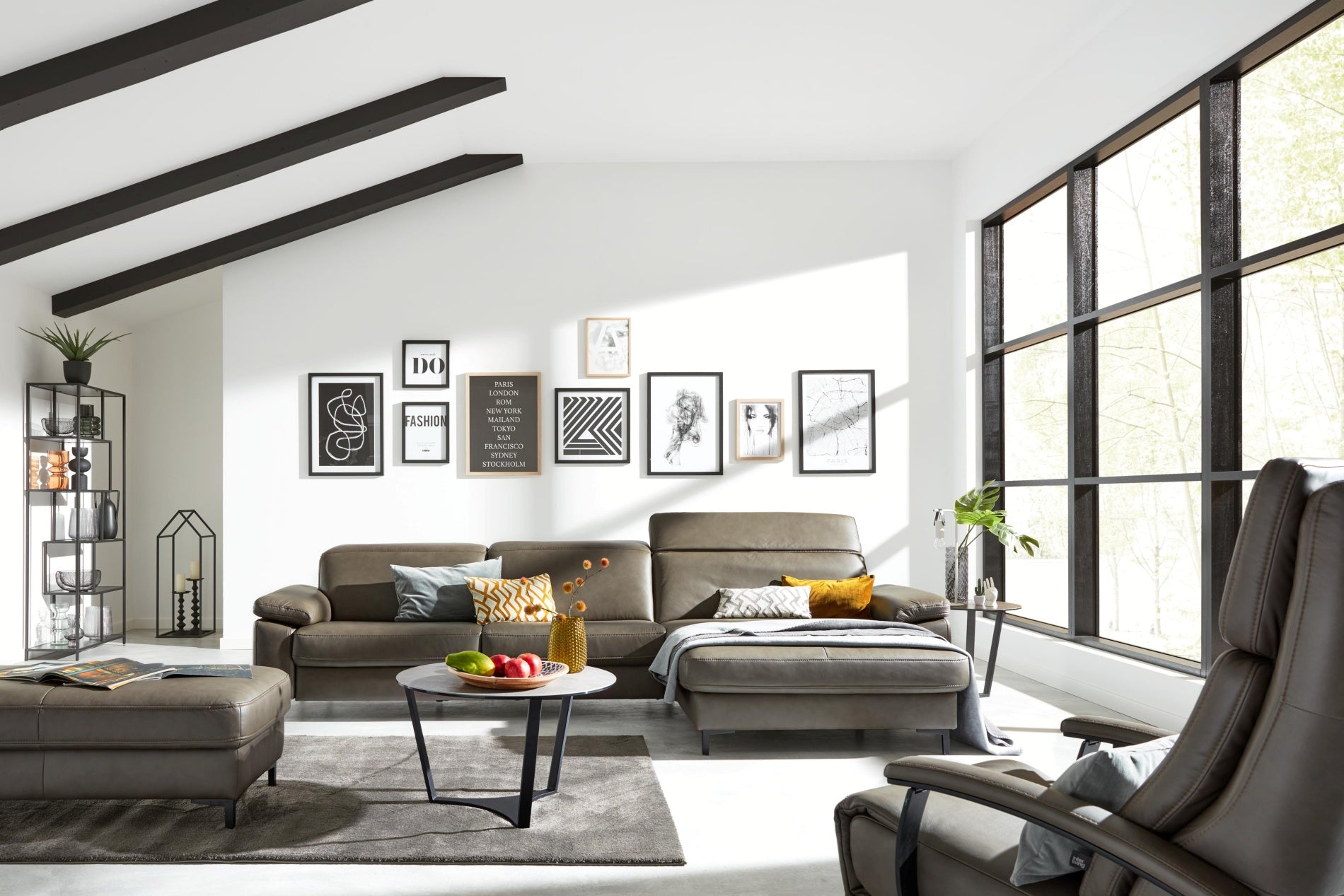 Modernes Wohnzimmer mit Ledersofas, Wandbildern, großen Fenstern und einem Couchtisch mit Obst und Deko.