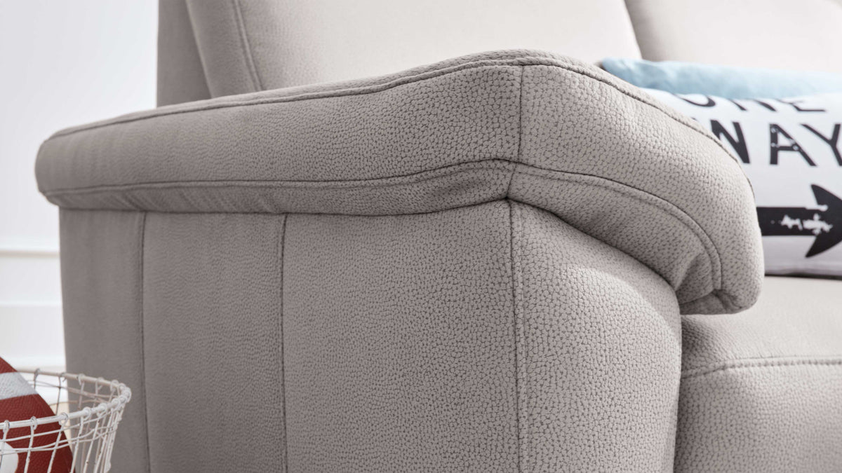 Ein graues Sofa mit strukturiertem Bezug, das einen weichen Armlehnenbereich zeigt, daneben liegt ein dekorisches Kissen.